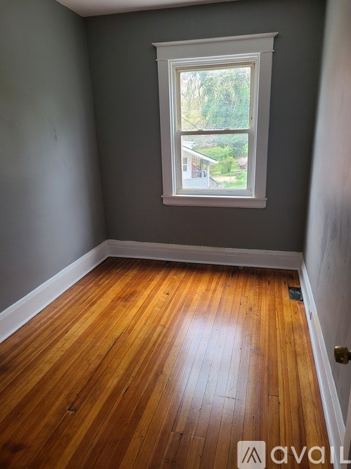 A room with wooden floors and a window showing a view of a house.