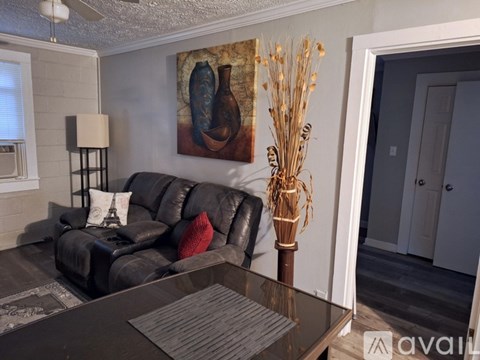 A living room with a black leather couch and a painting on the wall.