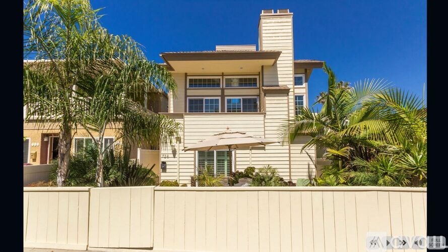 A house with a white fence and palm trees in front.