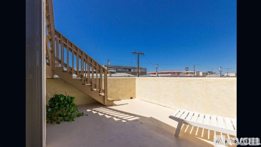A white bench is on a concrete patio with a staircase and a plant.