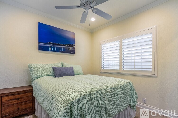 A bedroom with a bed, a ceiling fan, and a picture on the wall.