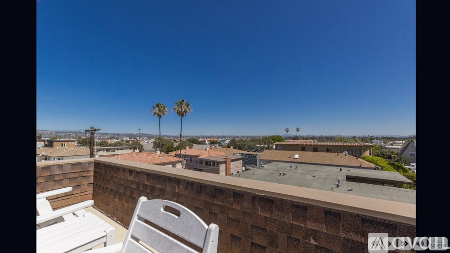 A white chair is on a balcony with a view of palm trees and buildings.