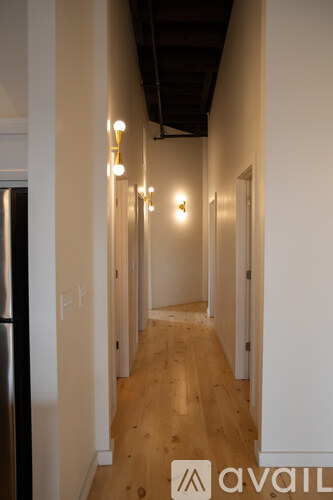 A long hallway with lights on the wall and a fridge on the left.