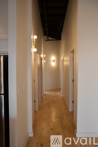A long hallway with lights on the wall and a fridge on the left.