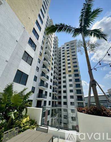A tall white building with balconies and a palm tree in front.