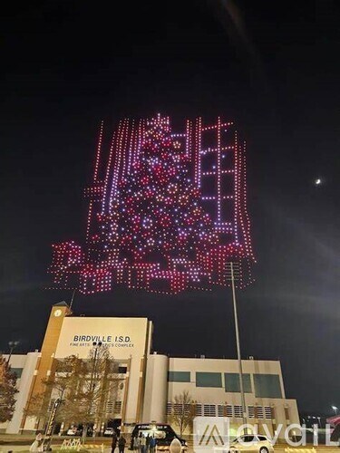 A large building with a sign that reads "Birdville ISD" is lit up with a large, colorful display.