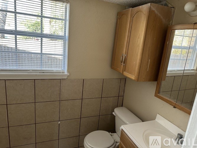 A bathroom with a toilet, sink, and a window with blinds.