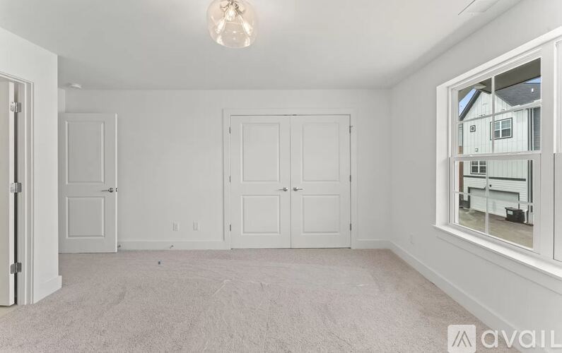 A room with white walls and a carpeted floor with a window showing a view of a house.