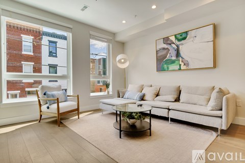 A living room with a white sofa, a wooden rocking chair, and a large abstract painting on the wall.