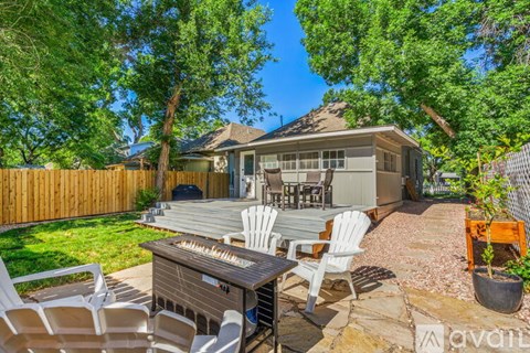 A backyard with a hot tub, chairs, and a house in the background.