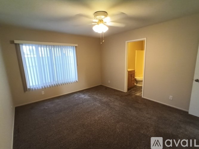 A room with a carpeted floor, a ceiling fan, and a window with blinds.