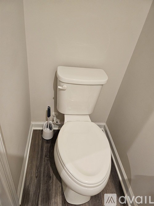 A white toilet with a toilet brush and a roll of toilet paper on a wooden floor.