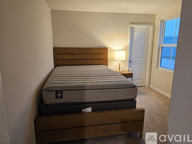 A bed with a wooden headboard and a single pillow is in a room with a window.