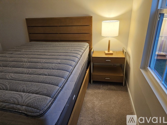 A bed with a grey cover and a wooden headboard is in a room with a carpeted floor.