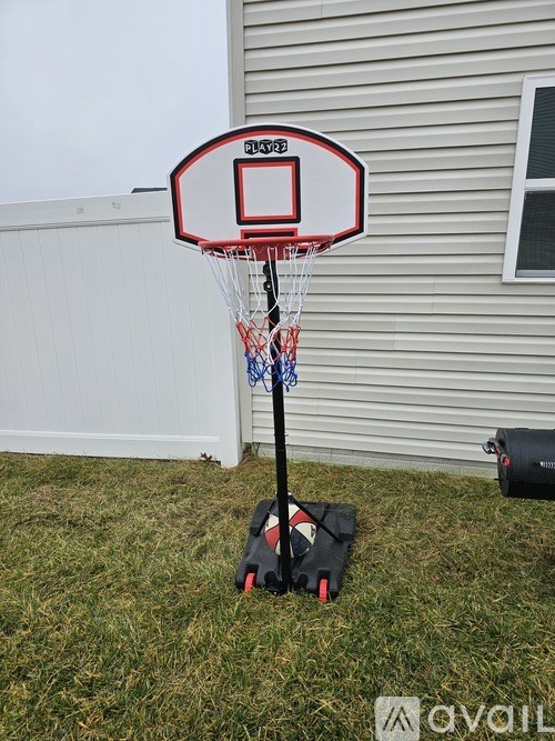 A portable basketball hoop is set up on a grassy area in front of a house.