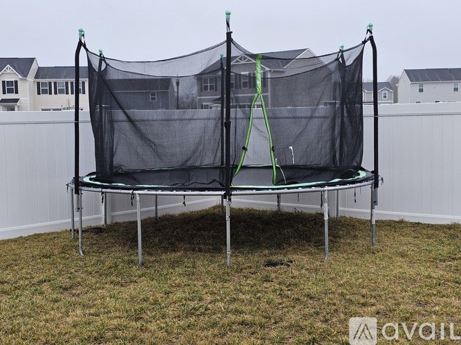 A trampoline with a safety net and padding is set up on a grassy area.