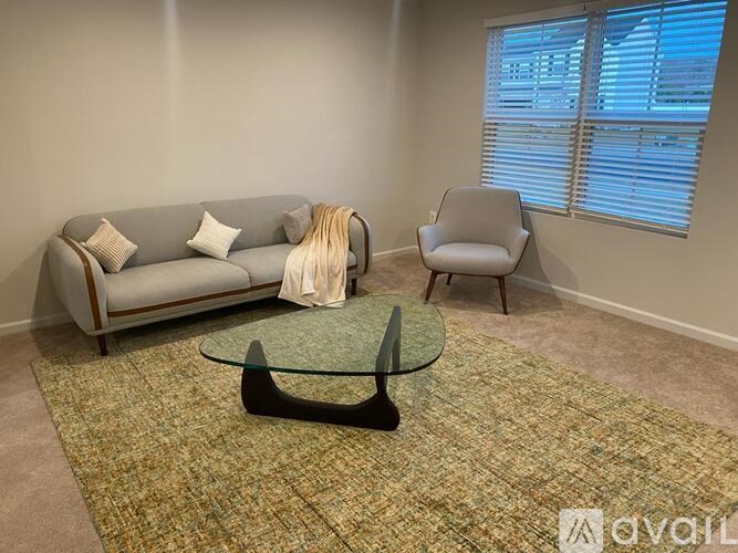 A living room with a grey couch, a glass coffee table, and a chair.