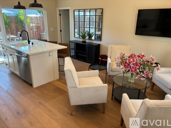 A living room with a white sofa, a white chair, and a glass coffee table with flowers on it.