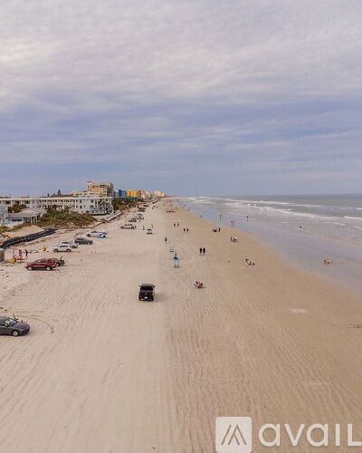 A beach scene with people and cars on the sand.