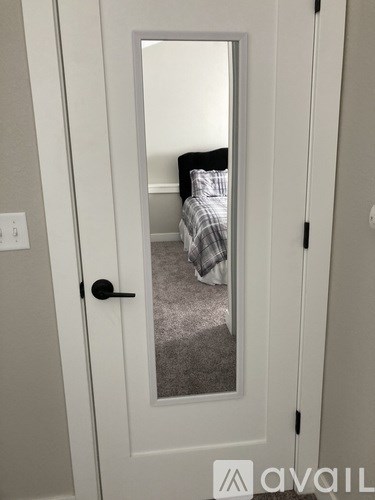 A white door with a mirror on it and a bedroom in the reflection.