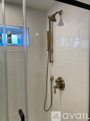A shower with a gold shower head and a gold valve.