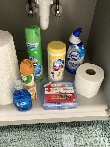 A bathroom shelf with toilet paper, cleaning supplies, and a box of wipes.