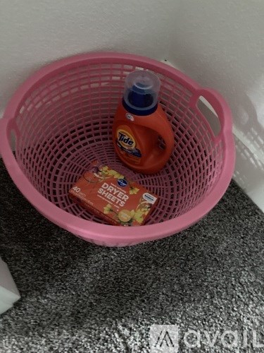 A pink laundry basket with a bottle of Tide detergent and a box of dryer sheets.
