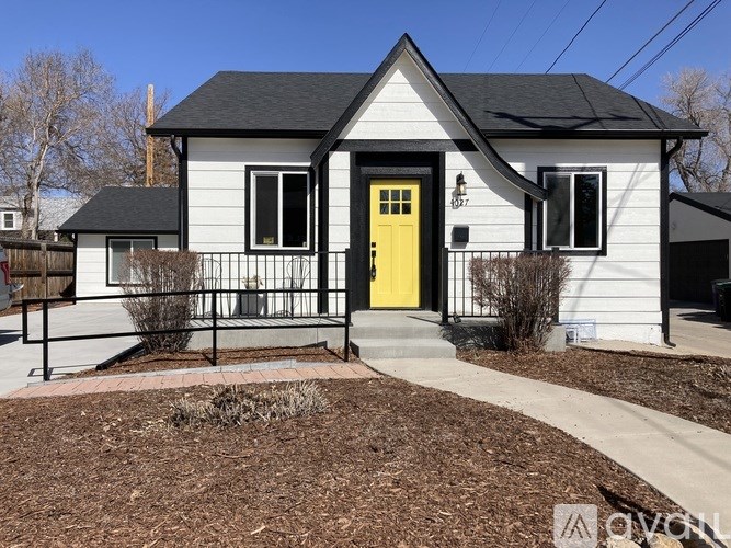 A small white house with a yellow door and black window frames.
