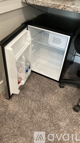 A small open fridge with a bottle of water and a bag of chips in it.