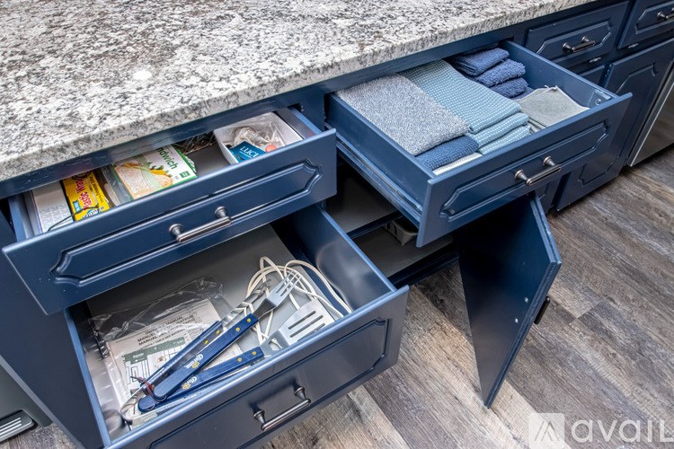 A kitchen drawer with a blue handle is open, revealing various items inside.