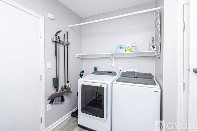 A kitchen with a white oven and microwave, a white shelf with cleaning supplies, and a white wall.