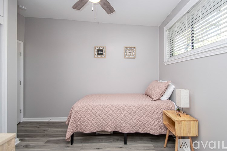 A bedroom with a pink bedspread and a wooden nightstand.