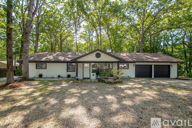 A house with a white exterior and a black roof is surrounded by trees.