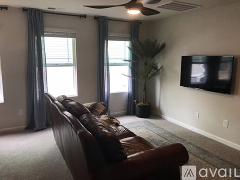 A living room with a brown leather couch and a flat screen TV mounted on the wall.