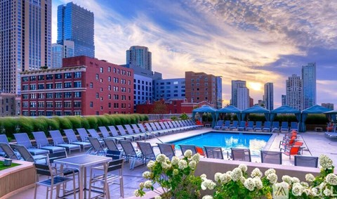 A rooftop pool area with lounge chairs and a table surrounded by buildings.