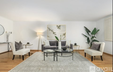 A living room with a grey rug and a glass table with a candle on it.