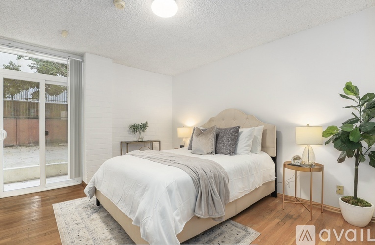 A bedroom with a large bed, a potted plant, and a lamp on a side table.