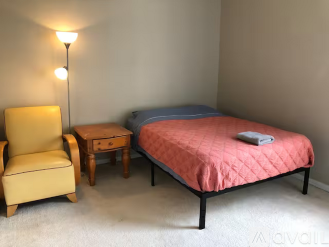 A bedroom with a bed, chair, and nightstand.