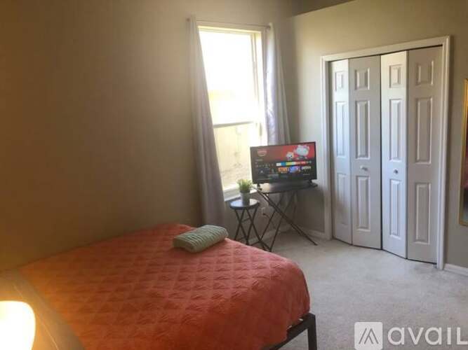 A bedroom with a bed, a small table with a TV on it, and a window with curtains.