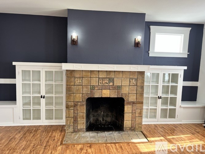 A fireplace with a black grate and a wooden mantle with glass doors.