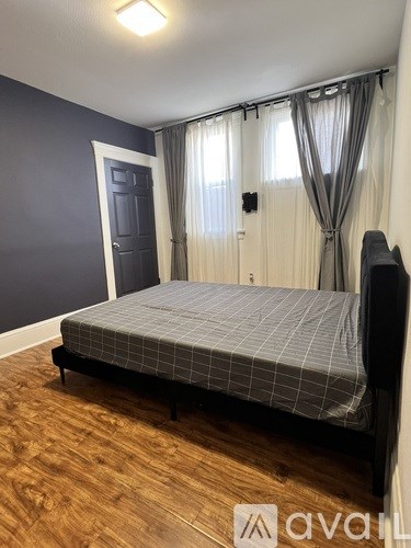 A bedroom with a bed, wooden floor, and a grey wall.