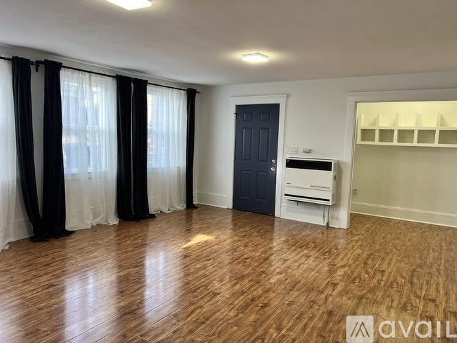 A room with wooden flooring, a black door, and a white cabinet.