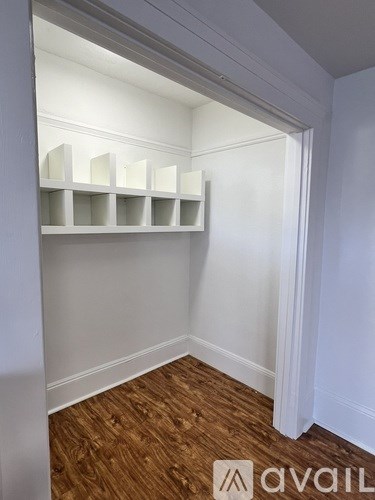 A white shelving unit with four shelves is in a corner of a room with wooden flooring.