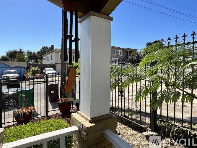 A white column stands on a porch with a black fence and plants in the background.