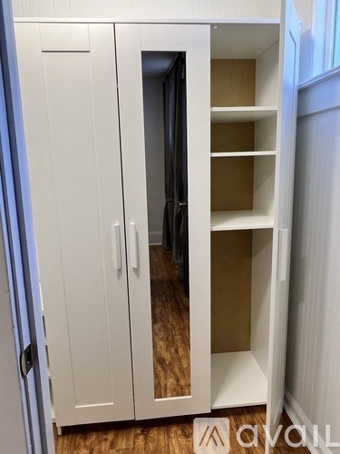 A white cabinet with a glass door is open, revealing shelves inside.