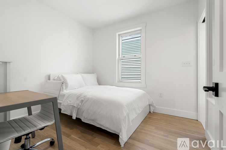A bedroom with a bed, a window with blinds, and a wooden floor.