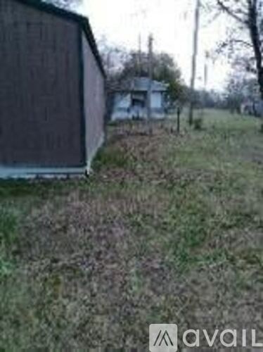 A grassy area with a shed and a house in the background.