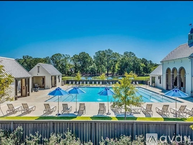 A pool area with chairs and umbrellas in front of a white building with a black roof.