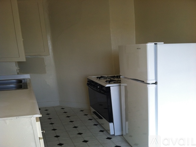 A kitchen with a white fridge, black and white tiled floor, and white cabinets.