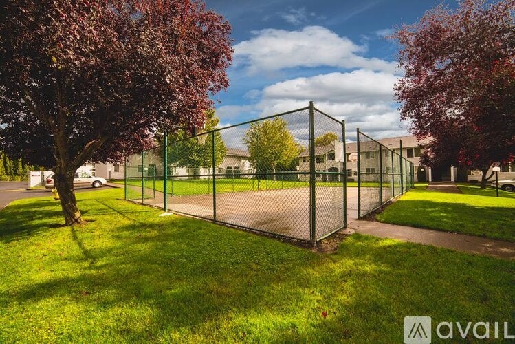 A tennis court surrounded by a green fence and trees.